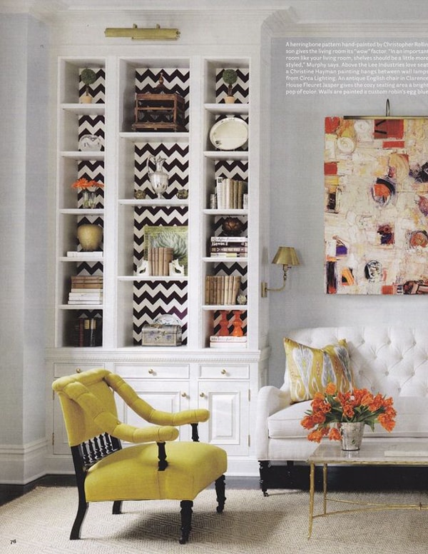 A beautifully styled bookcase with black and white striped wallpaper and vases, books, decorative plates and trinkets. 