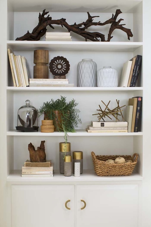 A bookcase styled with natural elements like decorative driftwood and woven baskets, stick sculptures, and plants. 