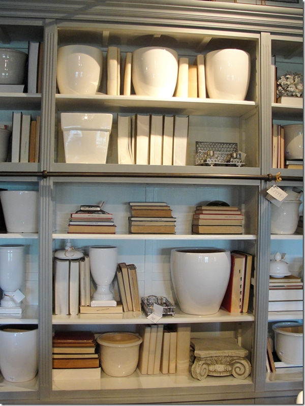This natural colored wood bookshelf is styled with old books that are desleeved and turned around to display the pages, along with white porcelain vases.