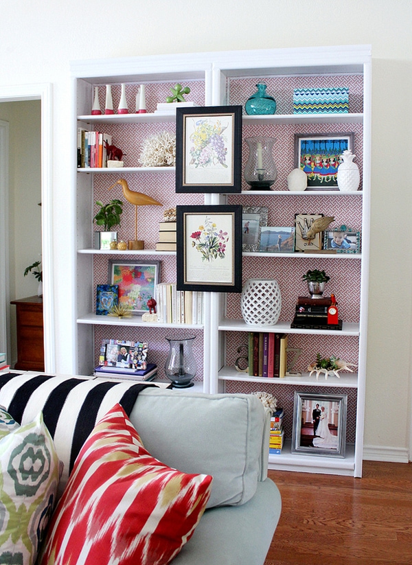 White double bookcase styled with artwork and collectables with a red and white patterned wallpaper background