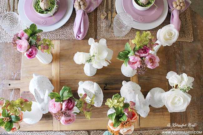 A beautiful and soft Easter table decor setting that is the perfect transition into spring. Soft whites with pops of flowers and pastels makes this Easter table setting perfect for your family! Check out more of this table on ablisfulnest.com