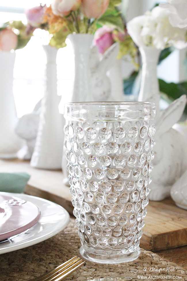 A beautiful and soft Easter table decor setting that is the perfect transition into spring. Soft whites with pops of flowers and pastels makes this Easter table setting perfect for your family! Check out more of this table on ablisfulnest.com