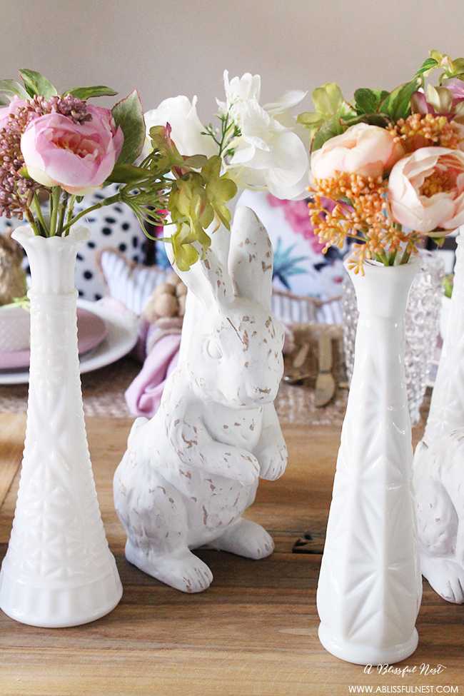A beautiful and soft Easter table decor setting that is the perfect transition into spring. Soft whites with pops of flowers and pastels makes this Easter table setting perfect for your family! Check out more of this table on ablisfulnest.com