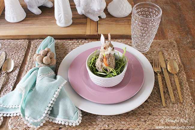 A beautiful and soft Easter table decor setting that is the perfect transition into spring. Soft whites with pops of flowers and pastels makes this Easter table setting perfect for your family! Check out more of this table on ablisfulnest.com