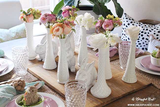 A beautiful and soft Easter table decor setting that is the perfect transition into spring. Soft whites with pops of flowers and pastels makes this Easter table setting perfect for your family! Check out more of this table on ablisfulnest.com