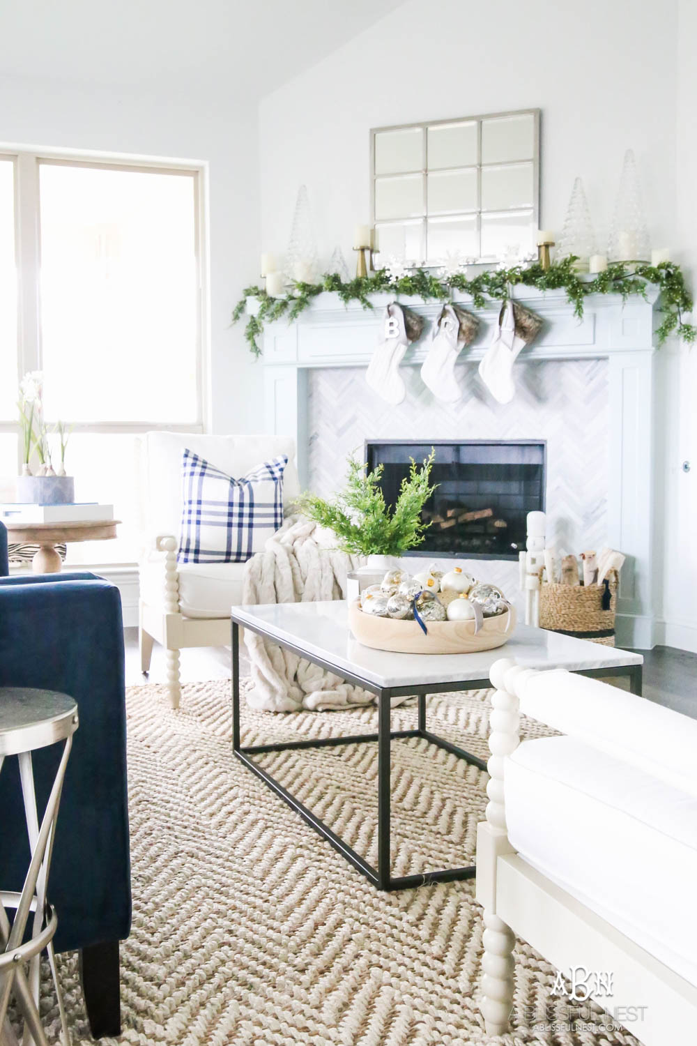 Gorgeous blue and silver Christmas mantle décor with juniper berry garland and glass hurricane Christmas trees. Simple and festive holiday décor in this open concept living space. Check out all the white, silver and gold Christmas decor in this holiday home tour on ablisfulnest.com. #ABlissfulNest #Christmasdecor #Christmasdecorating #CoastalChristmasdecor #christmastree #christmasmantle