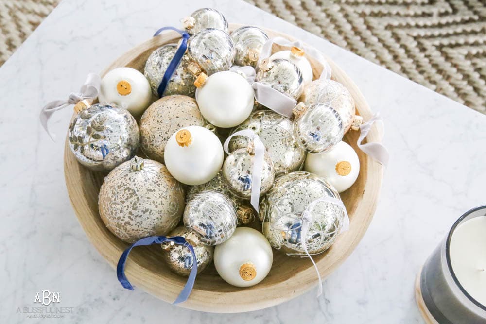Mercury glass ornaments with velvet ribbons tied and collected in a wood bowl on a coffee table for a gorgeous holiday décor display. Simple touches for Christmas décor that make big impact. Check out all the white, silver and gold Christmas decor in this holiday home tour on ablisfulnest.com. #ABlissfulNest #Christmasdecor #Christmasdecorating #CoastalChristmasdecor #christmastree #christmasmantle