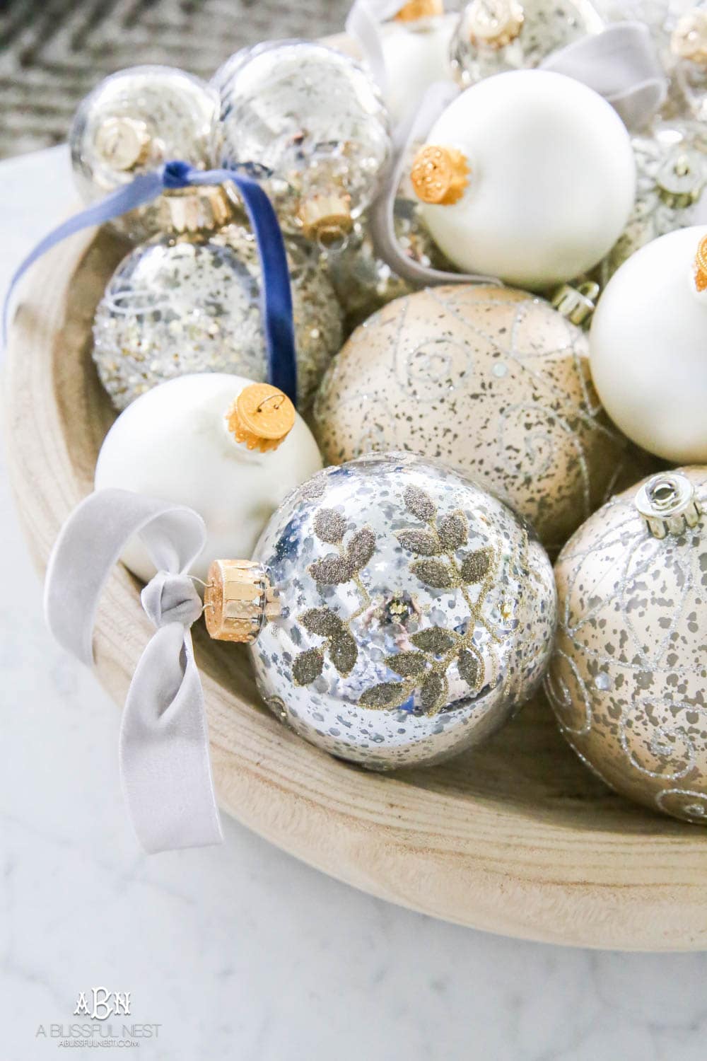 Mercury glass ornaments with velvet ribbons tied and collected in a wood bowl on a coffee table for a gorgeous holiday décor display. Simple touches for Christmas décor that make big impact. Check out all the white, silver and gold Christmas decor in this holiday home tour on ablisfulnest.com. #ABlissfulNest #Christmasdecor #Christmasdecorating #CoastalChristmasdecor #christmastree #christmasmantle
