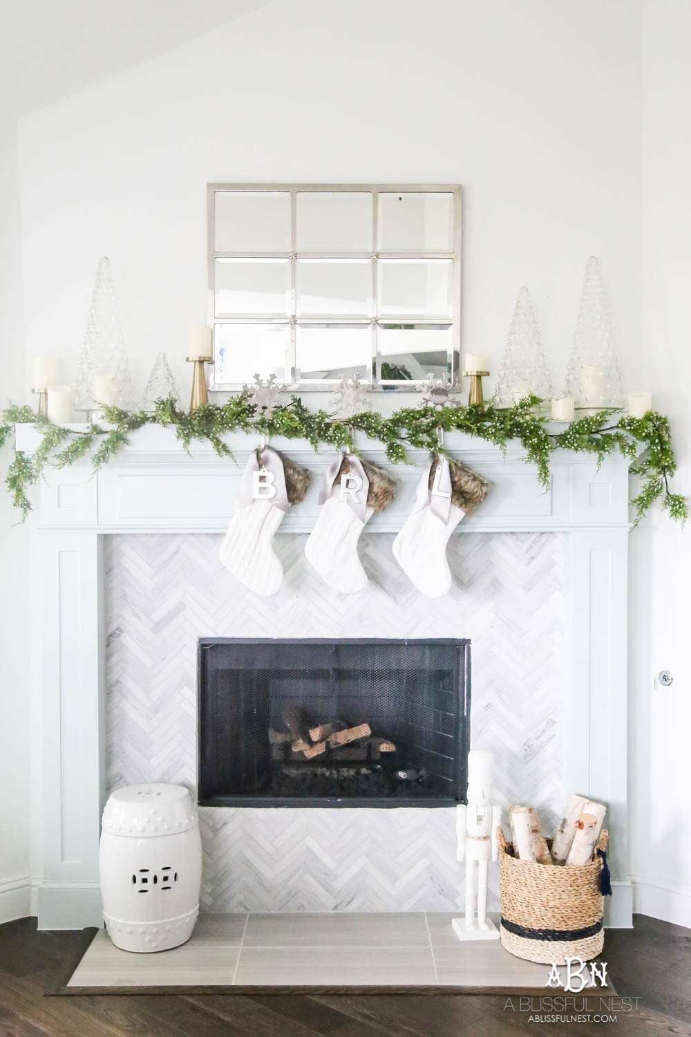 Gorgeous blue and silver Christmas mantle décor with juniper berry garland and glass hurricane Christmas trees. Simple and festive holiday décor in this open concept living space. Check out all the white, silver and gold Christmas decor in this holiday home tour on ablisfulnest.com. #ABlissfulNest #Christmasdecor #Christmasdecorating #CoastalChristmasdecor #christmastree #christmasmantle