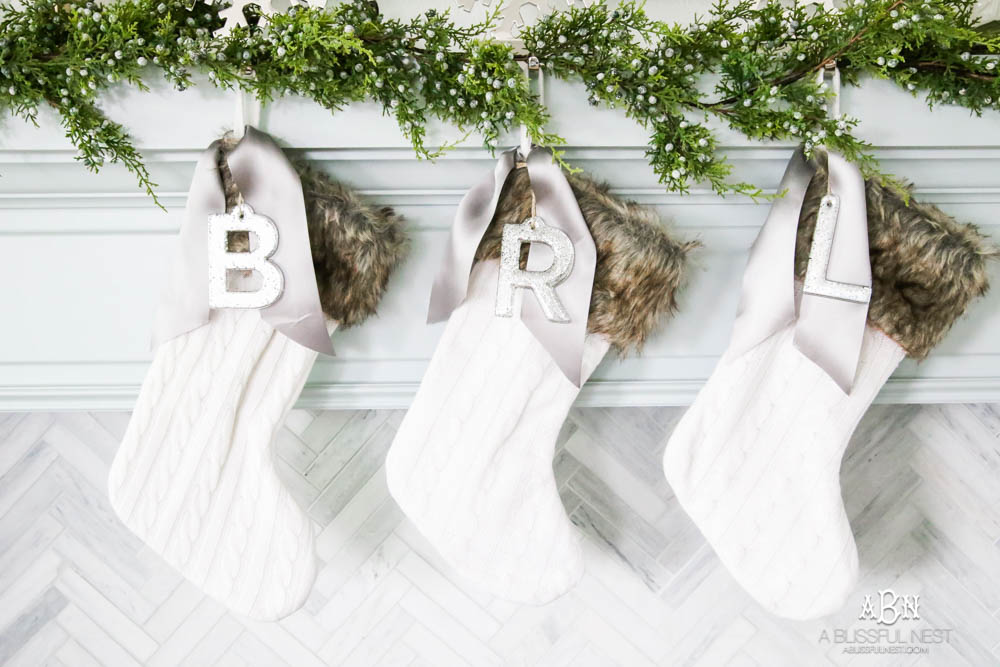 Gorgeous blue and silver Christmas mantle décor with juniper berry garland and glass hurricane Christmas trees. Simple and festive holiday décor in this open concept living space. Check out all the white, silver and gold Christmas decor in this holiday home tour on ablisfulnest.com. #ABlissfulNest #Christmasdecor #Christmasdecorating #CoastalChristmasdecor #christmastree #christmasmantle