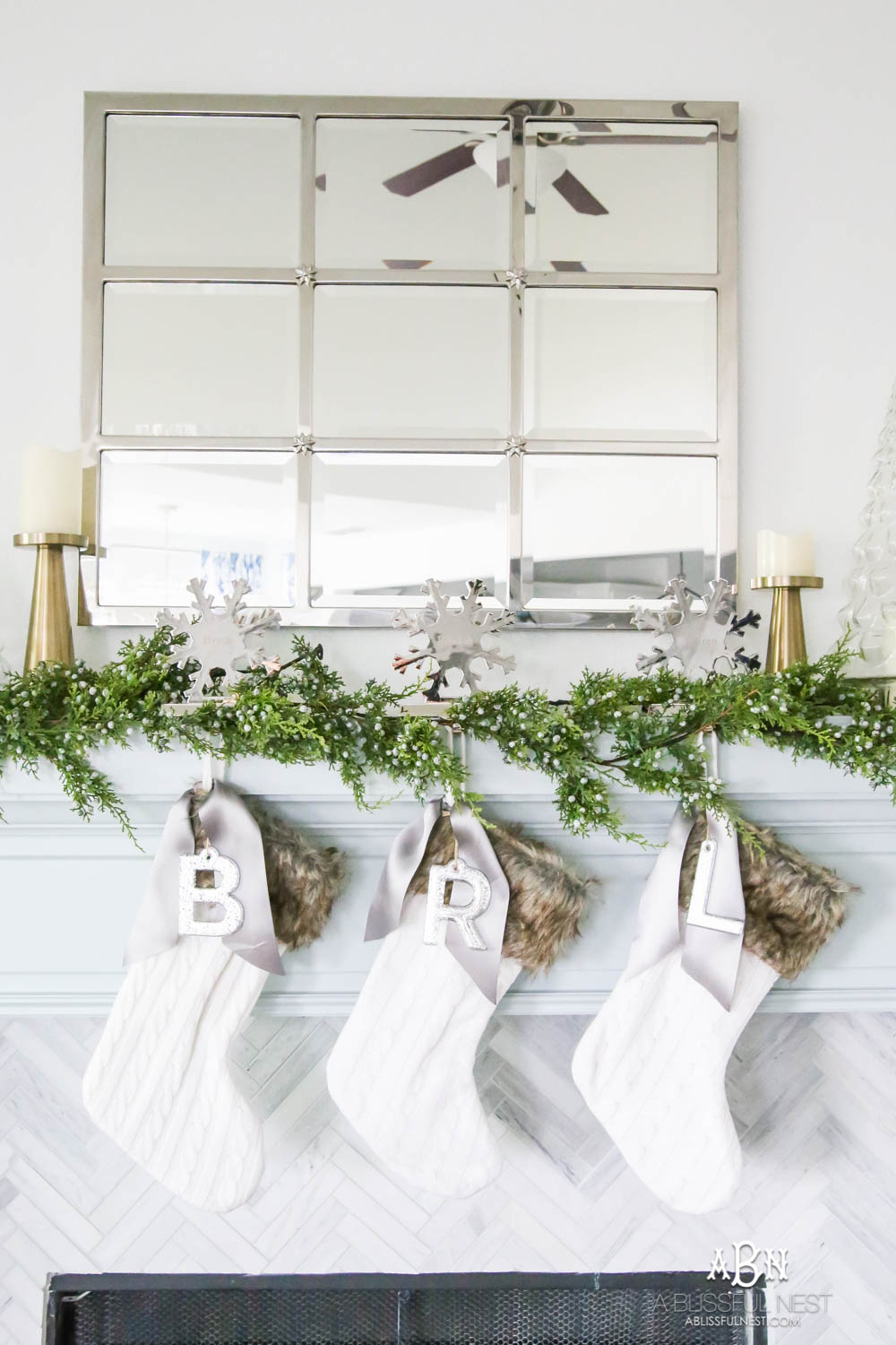 Gorgeous blue and silver Christmas mantle décor with juniper berry garland and glass hurricane Christmas trees. Simple and festive holiday décor in this open concept living space. Check out all the white, silver and gold Christmas decor in this holiday home tour on ablisfulnest.com. #ABlissfulNest #Christmasdecor #Christmasdecorating #CoastalChristmasdecor #christmastree #christmasmantle