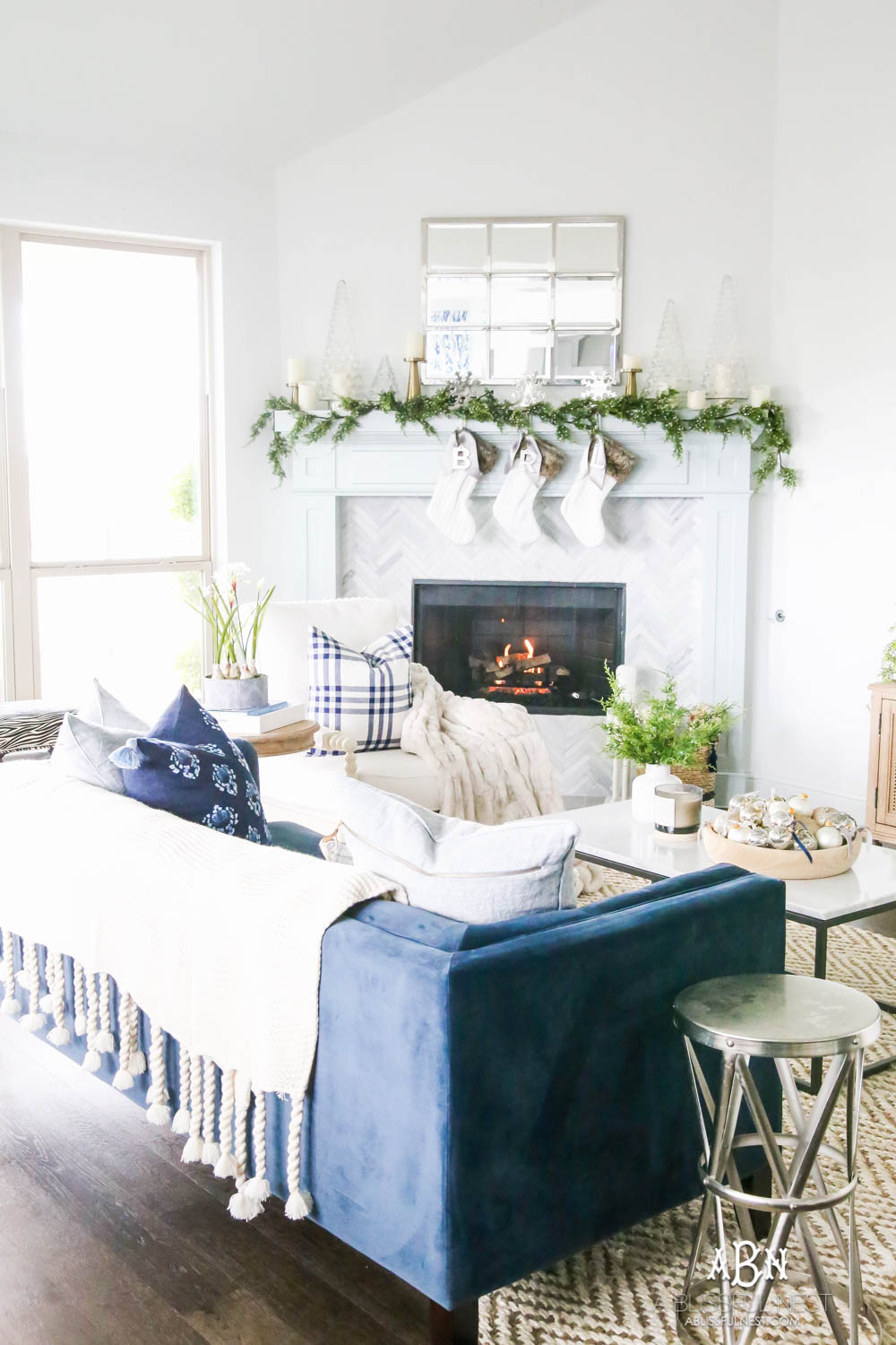 Gorgeous blue and silver Christmas mantle décor with juniper berry garland and glass hurricane Christmas trees. Simple and festive holiday décor in this open concept living space. Check out all the white, silver and gold Christmas decor in this holiday home tour on ablisfulnest.com. #ABlissfulNest #Christmasdecor #Christmasdecorating #CoastalChristmasdecor #christmastree #christmasmantle