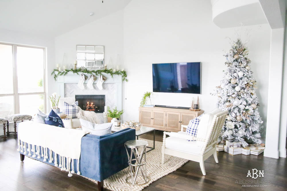 Beautiful blue and silver Christmas living room decor in a bright white space with juniper garland and silver and blush ornaments. Check out all the white, silver and gold Christmas decor in this holiday home tour on ablisfulnest.com. #ABlissfulNest #Christmasdecor #Christmasdecorating #CoastalChristmasdecor #christmastree #christmasmantle