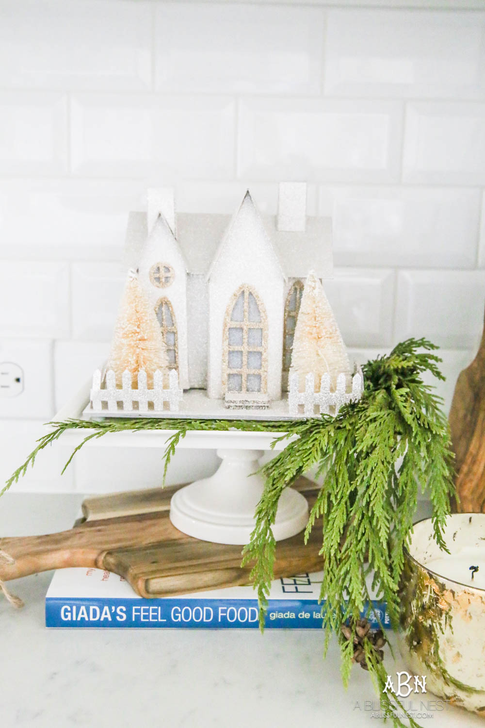Blue and silver Christmas kitchen décor. All white kitchen with subtle holiday décor for a fresh coastal Christmas look. Mini wreaths on the backs of the barstools, beautiful bay leaf above the range. #christmaskitchen #christmashometour #holidayhometour #kitchenideas