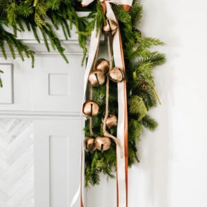 Gold bells and ribbons tied to the side of a garland on a fireplace mantle