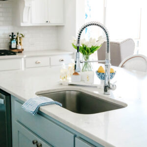 View of kitchen sink with soft blue cabinet color with a vase of white tulips.
