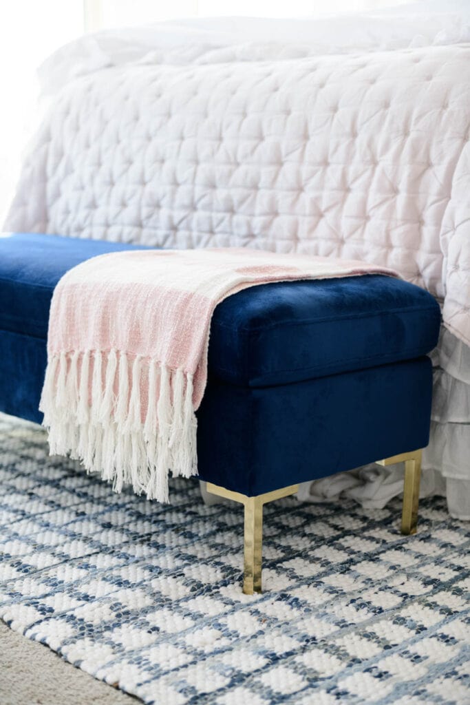 Navy blue velvet ottoman with pink and white tassel blanket draped over the end.