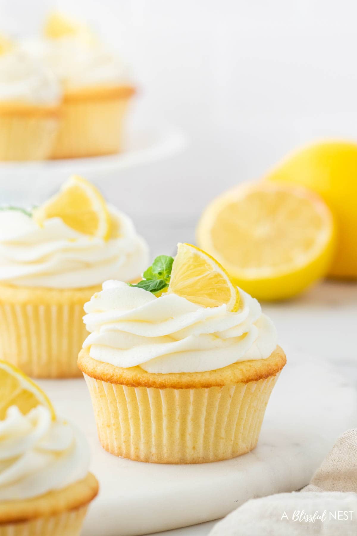 Lemon cupcake with a cream cheese frosting and decorated with a slice of lemon and mint.