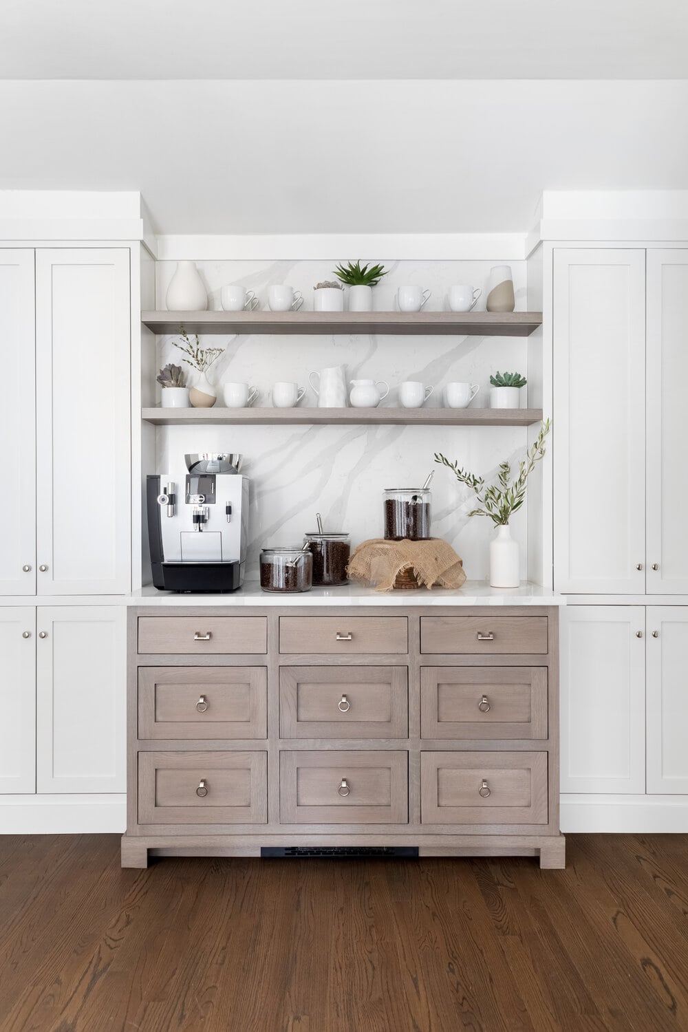 Coffee station created from a builtin section of cabinetry. Coffee maker, white coffee cups, canisters with coffee beans.