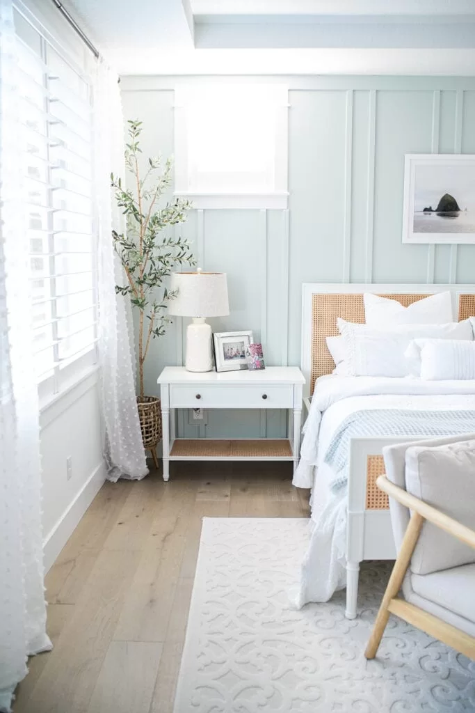 board and batten walls, sea green painted walls, cane headboard, olive tree in basket next to window.