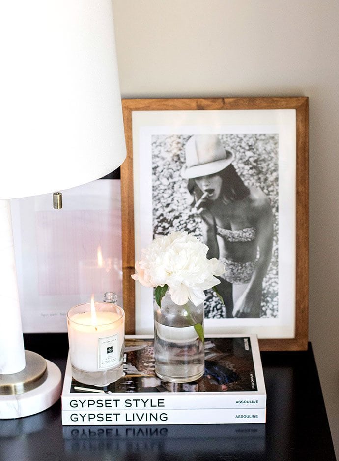 coffee table books on a nightstand with a candle and vase of flowers. 