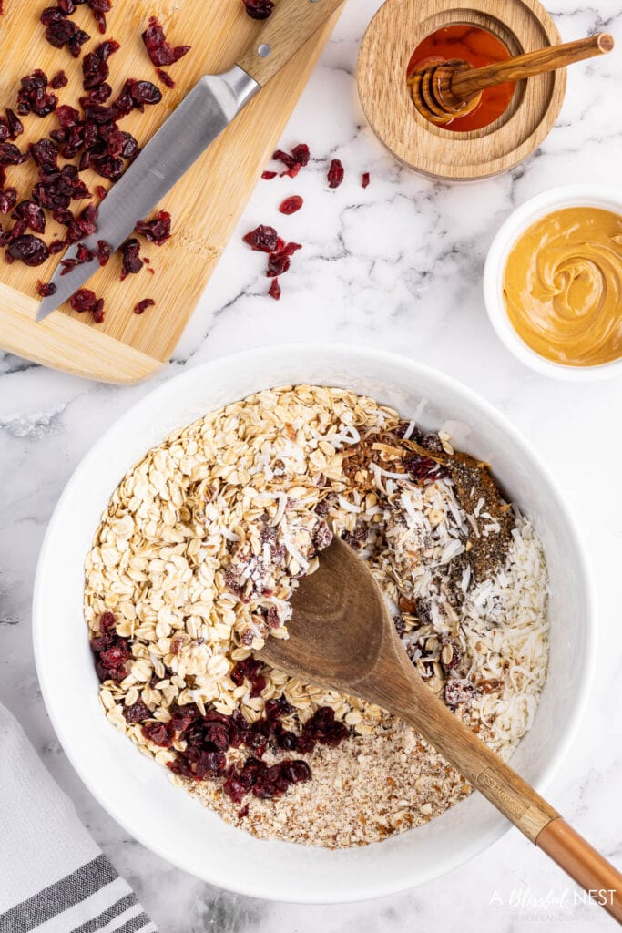 white bowl on countertop with of the ingredients added and being stirred with a wooden spoon to make the energy balls.