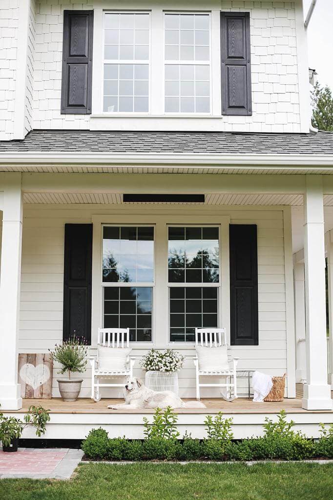 Two white rocking chairs on a front porch with a lavender tree in a pot and a basket with a white blanket.