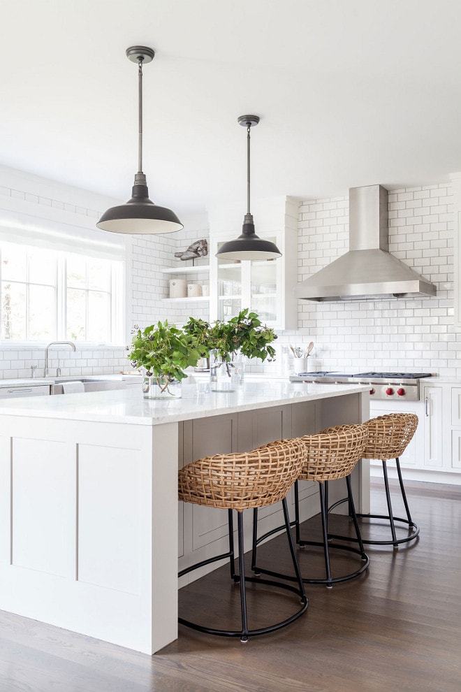 light cream kitchen island with woven barstools with black iron legs, white kitchen cabinets, stainless steel range hood.
