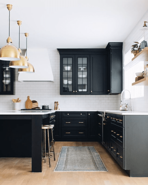 Black kitchen cabinets with white range hood, gold dome pendant lights, oak flooring