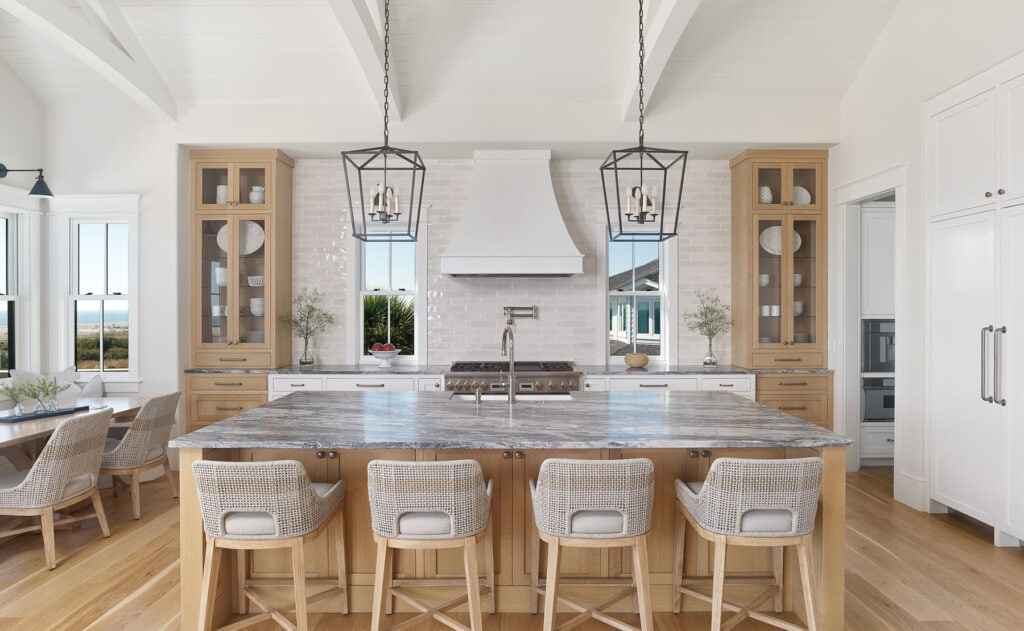 Honey oak kitchen cabinets, white hood, woven barstools, black lantern pendents over island
