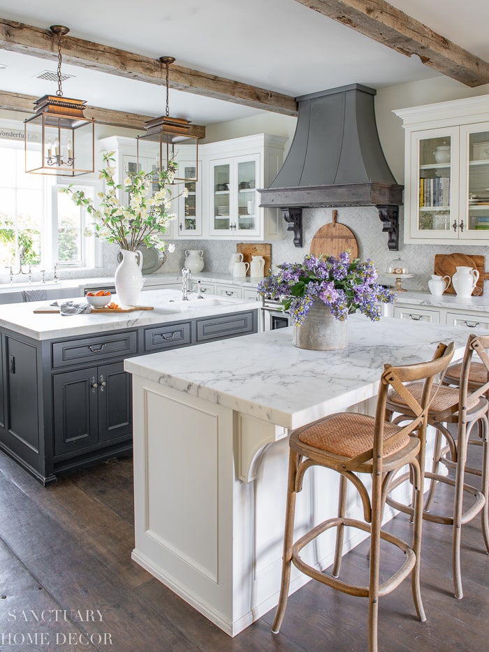 grey kitchen island and range hood, wood farmhouse barstools, gold lantern pendant lights above island, marble countertops