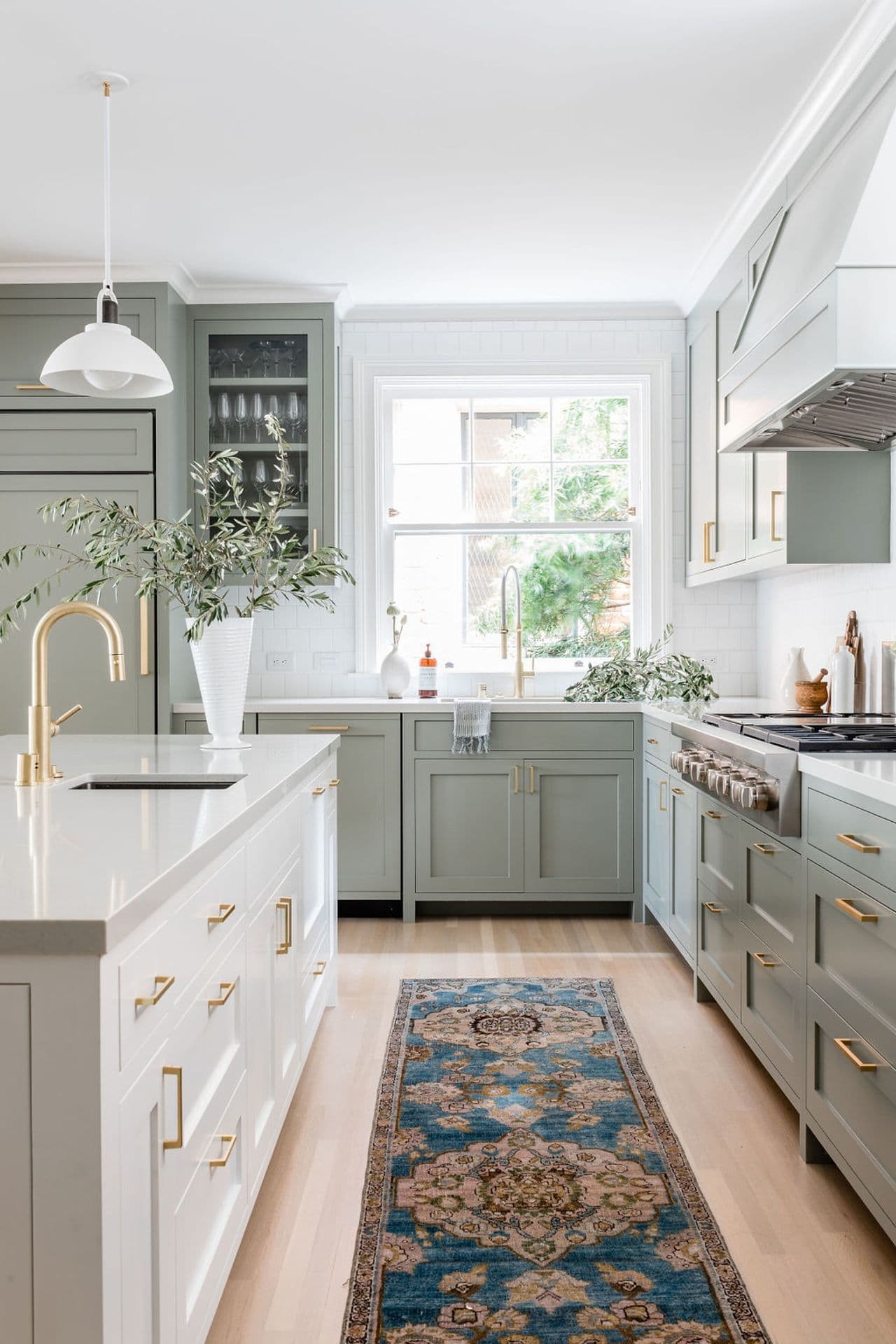 sage green kitchen cabinets with gold cabinet hardware, window behind sink, gold faucets