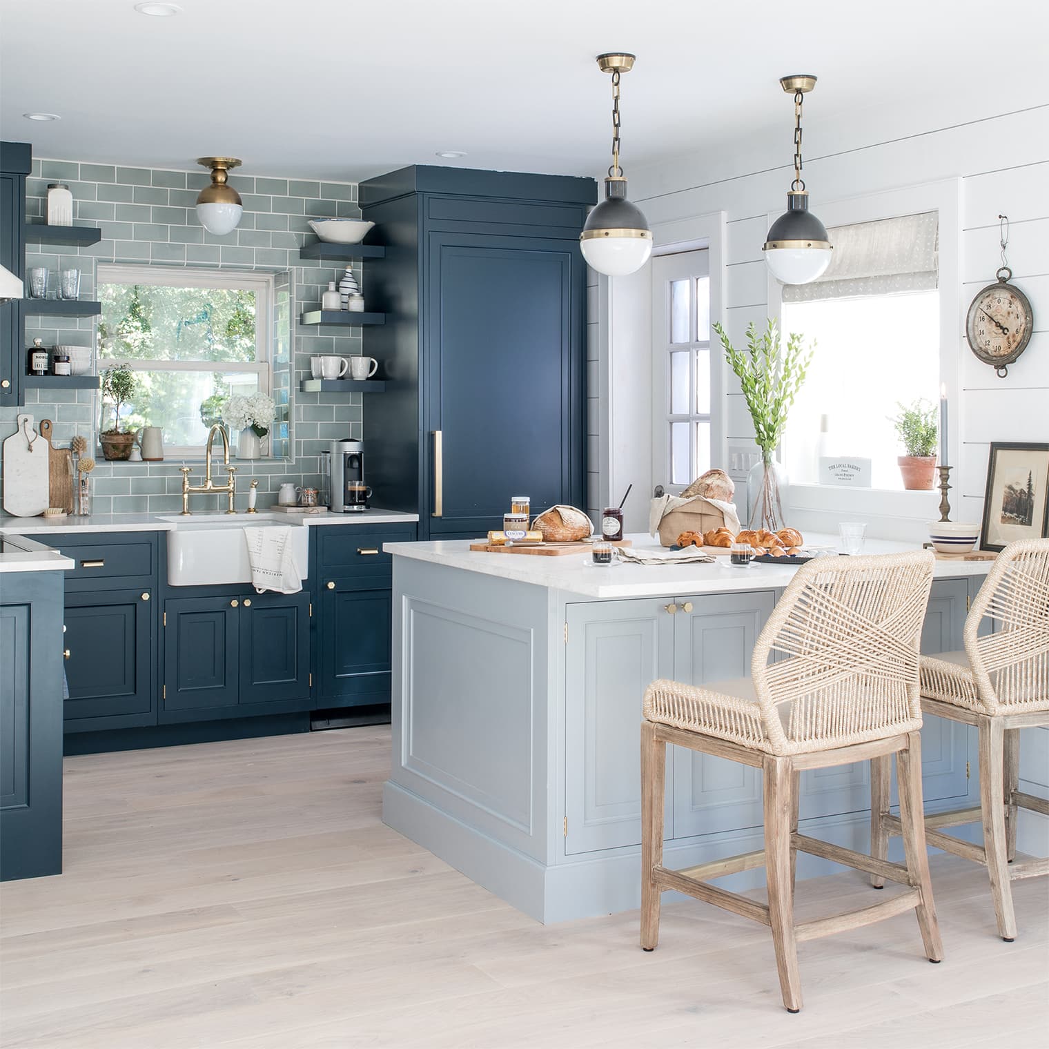 light blue kitchen island black and gold globe pendants, woven barstools, light wood floor.