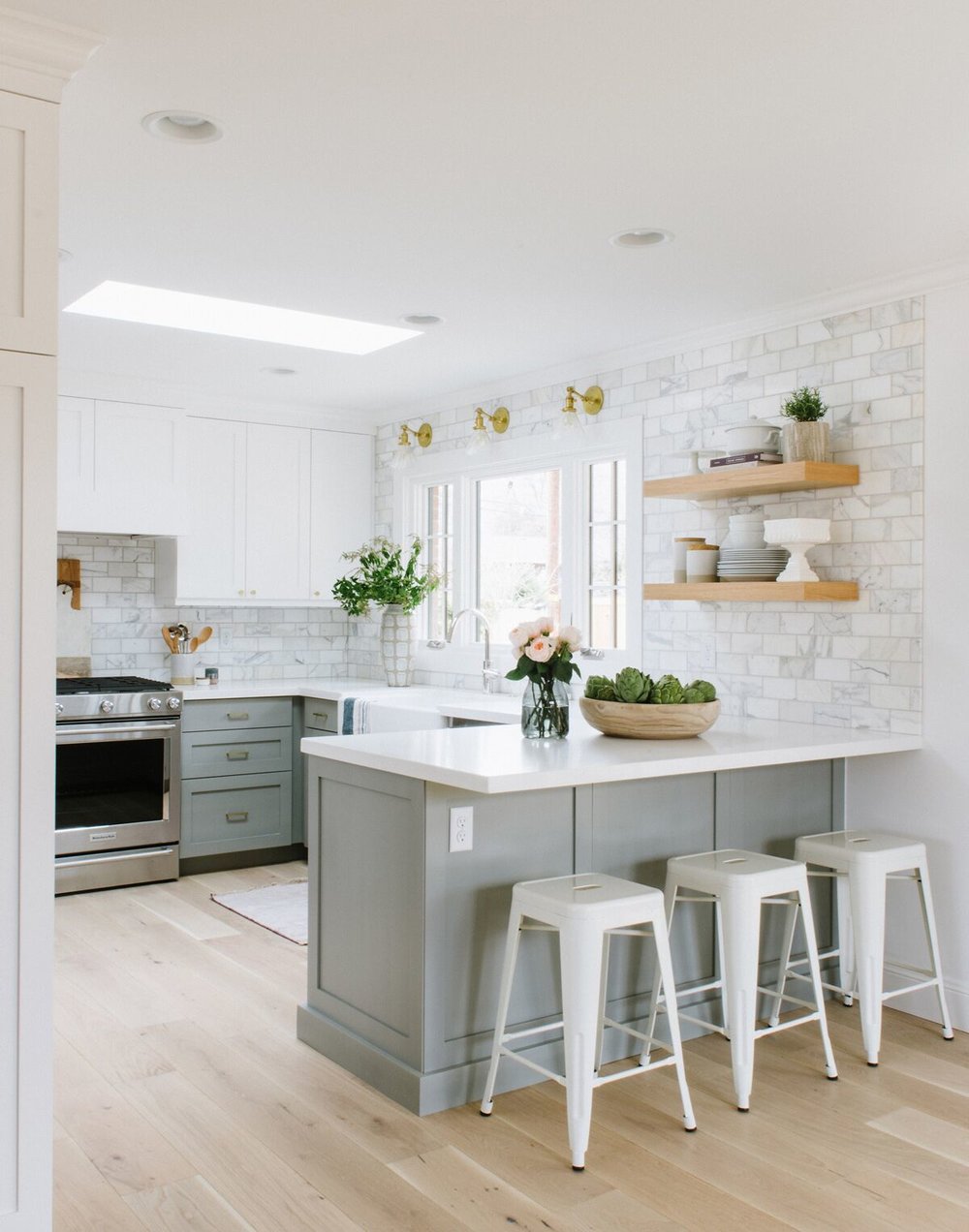 Light grey lower cabinets withe white upper cabinets and wood floating shelves. Marble subway tiles.