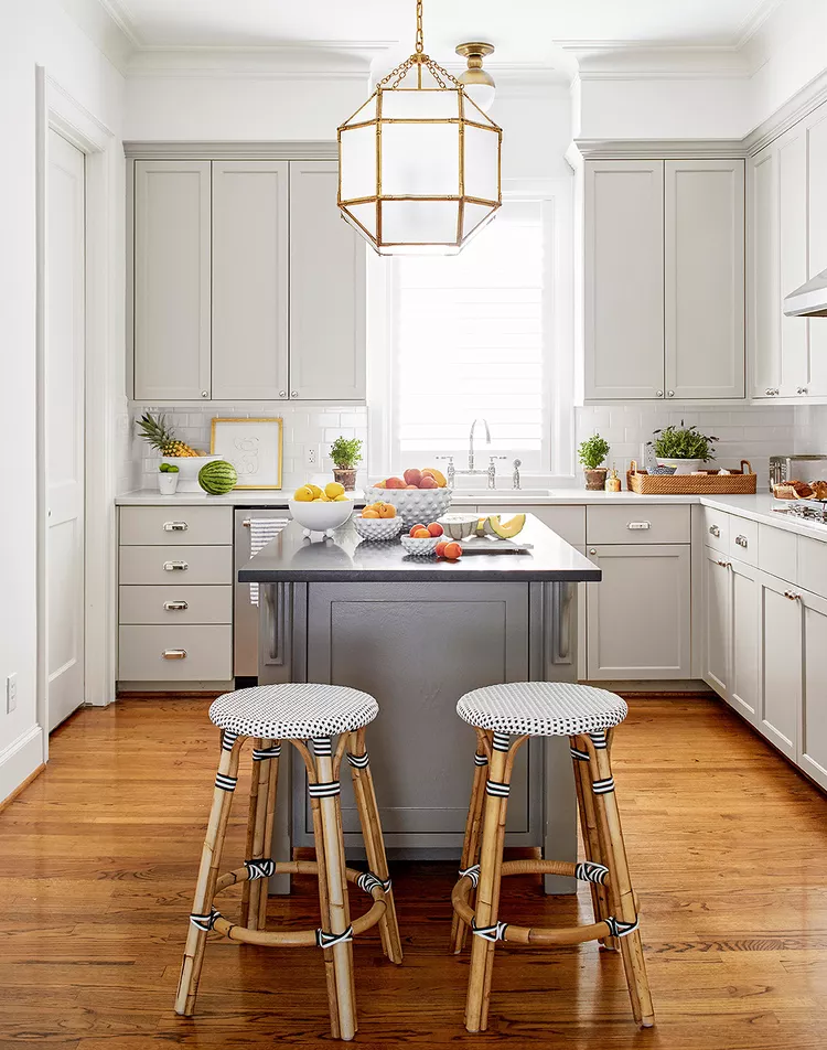 dark grey island with light grey perimeter cabinets, chrome cabinet hardware, window over the sink.