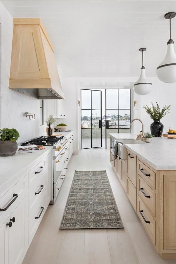light wood hood and island with black cabinet hardware. White perimeter base cabinets. 