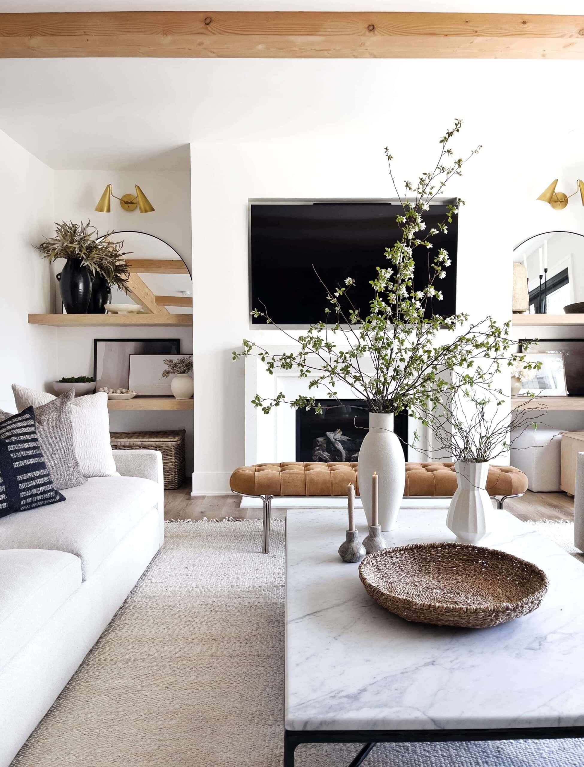 Crips white living room with tan and beige decor accents. Features gold sconces.