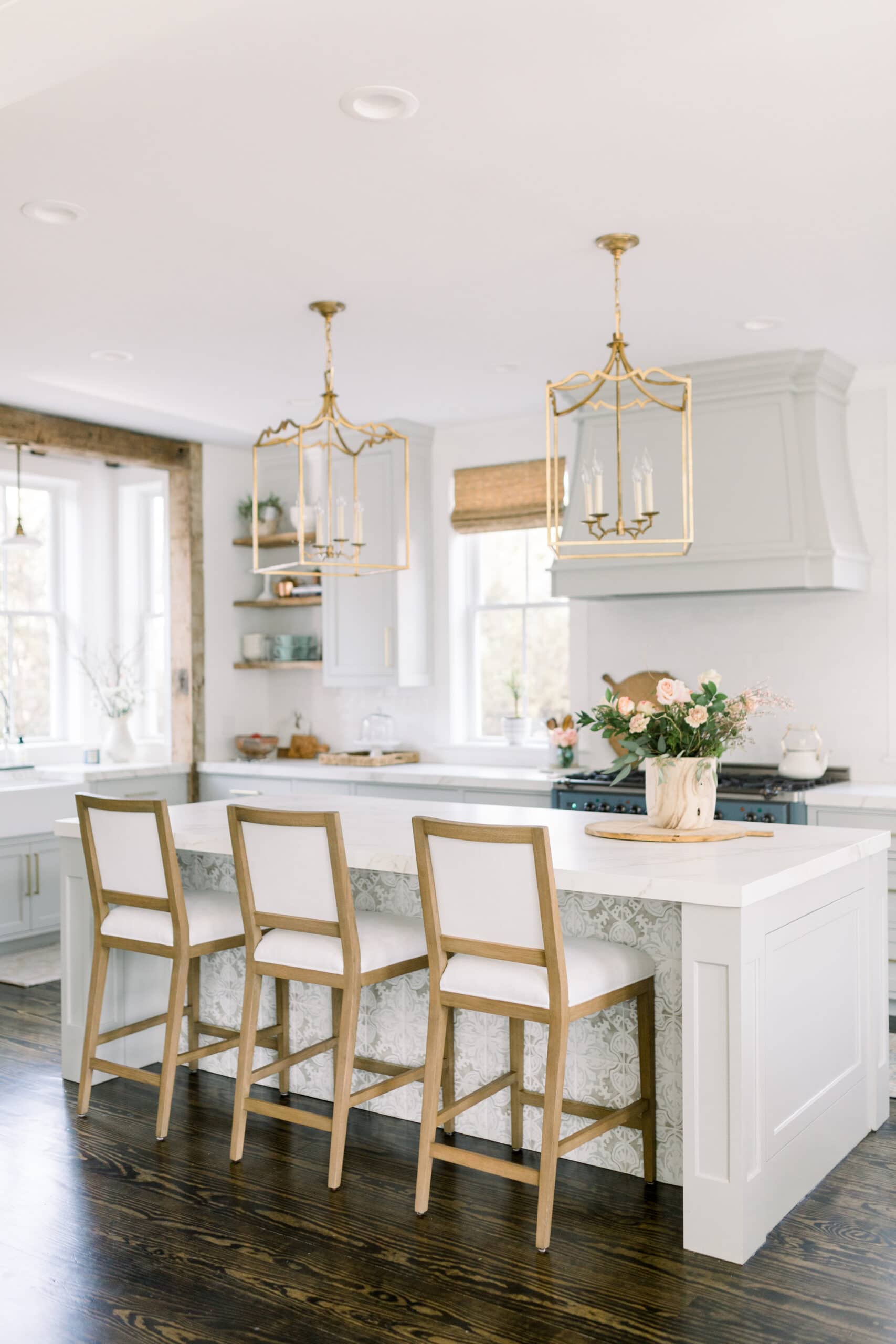 hrey kitchen cabinets, gold lantern pendants, wood upholstered barstools, bamboo shades on windows
