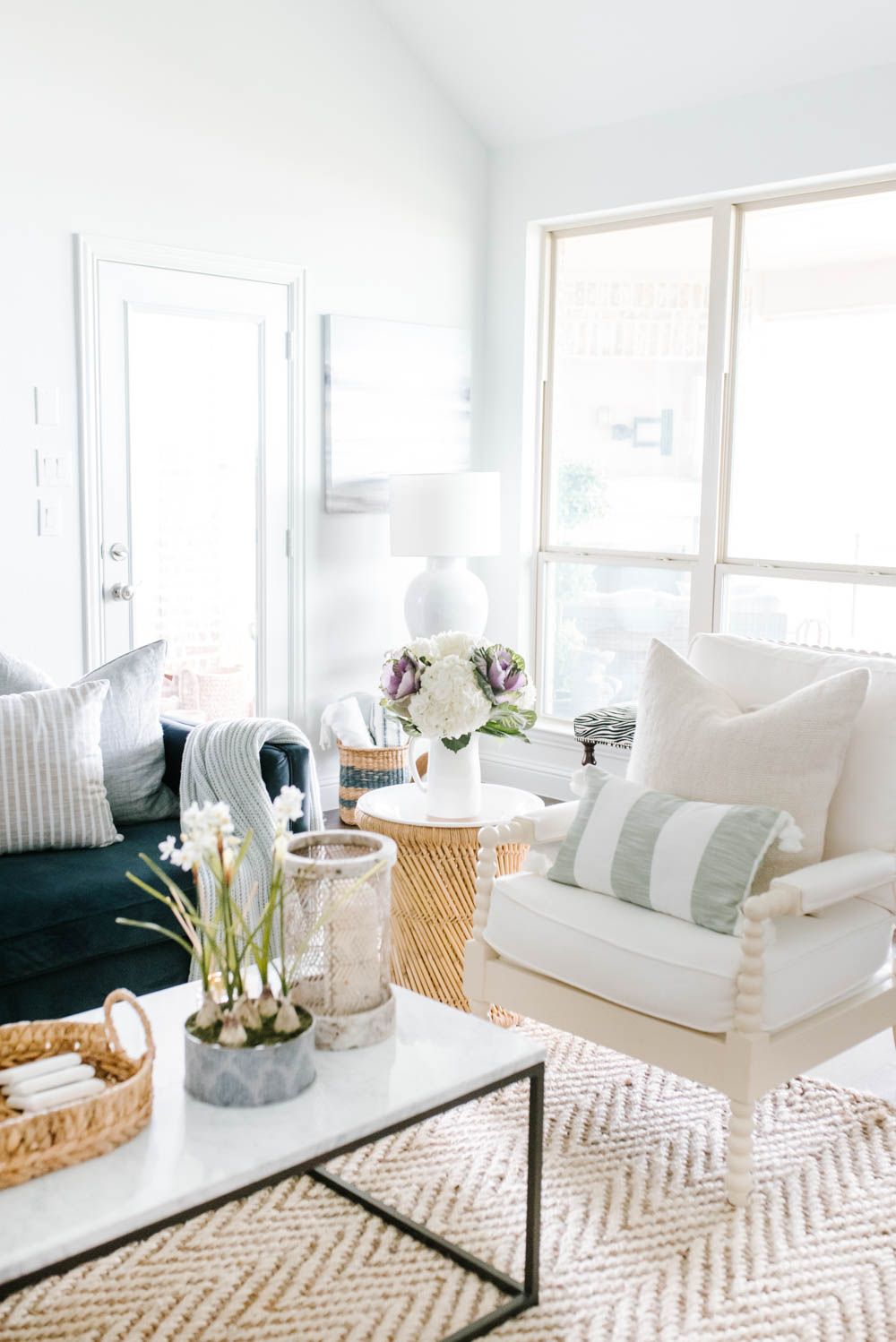 white spindle chair with linen pillow, soft green and white striped pillow next to blue sofa with light blue pillow and grey and white striped pillow
