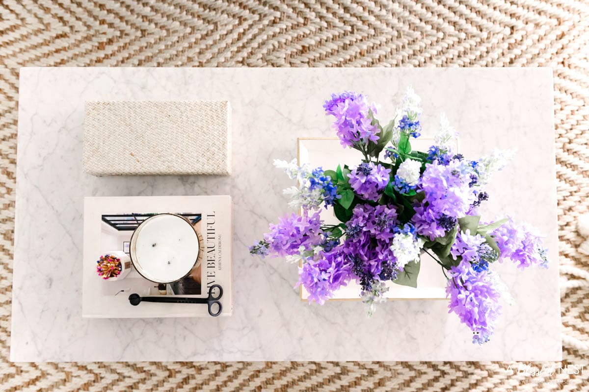 Flowers, decorative books, candles, and a small box decorate a coffee table.