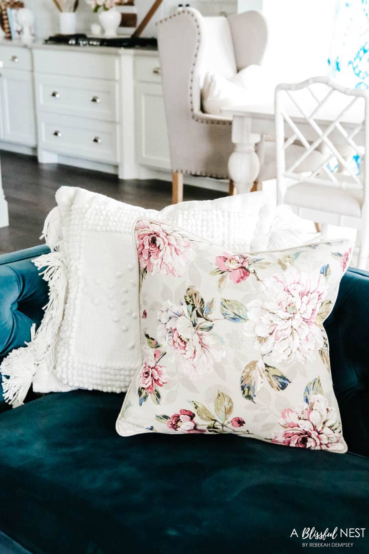 textured white pillow with fringe paired with a  tan and cream floral pillow with light pink and dark pink flowers.