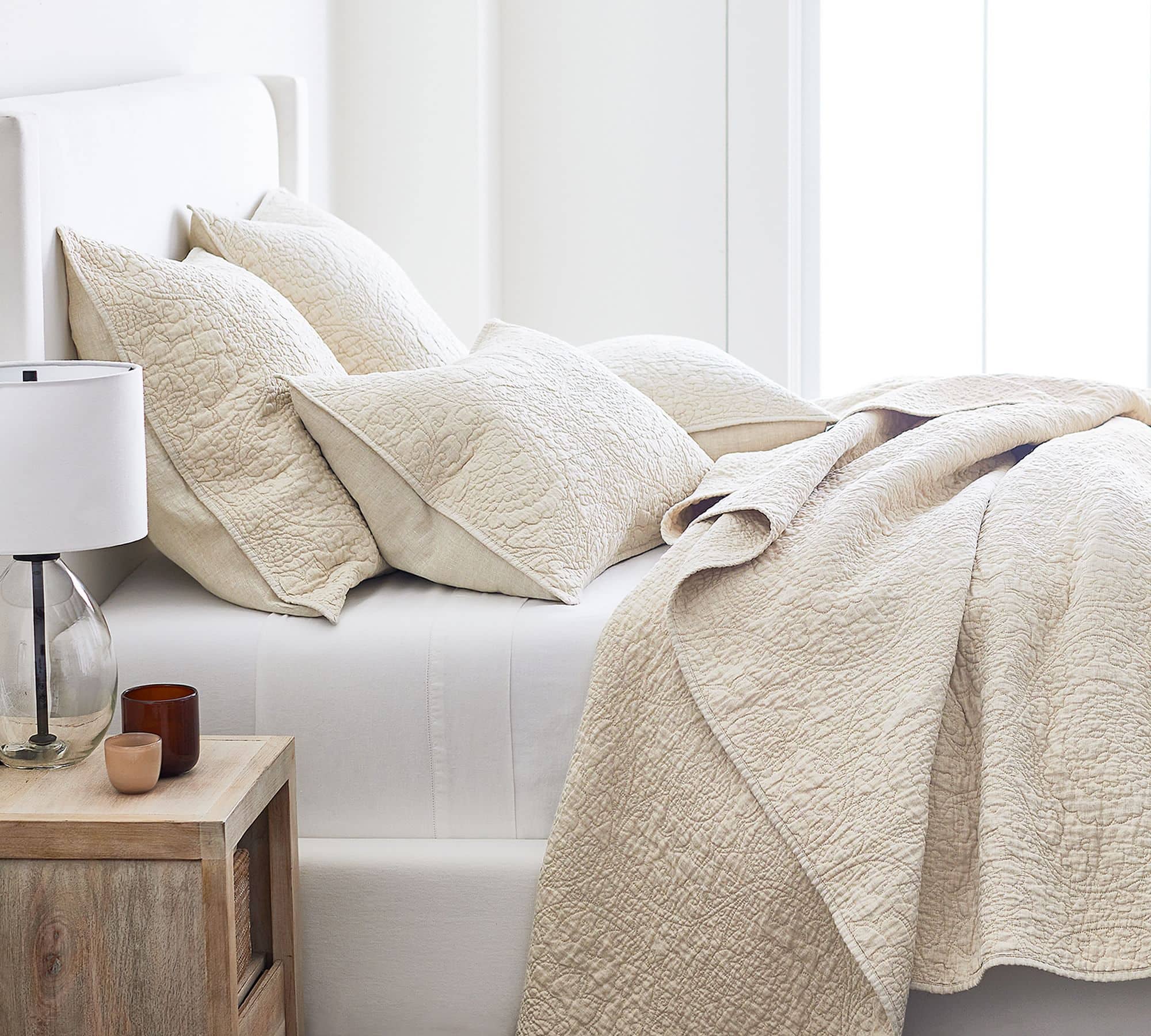 beige quilted coverlet with white bedding on a white upholstered bed