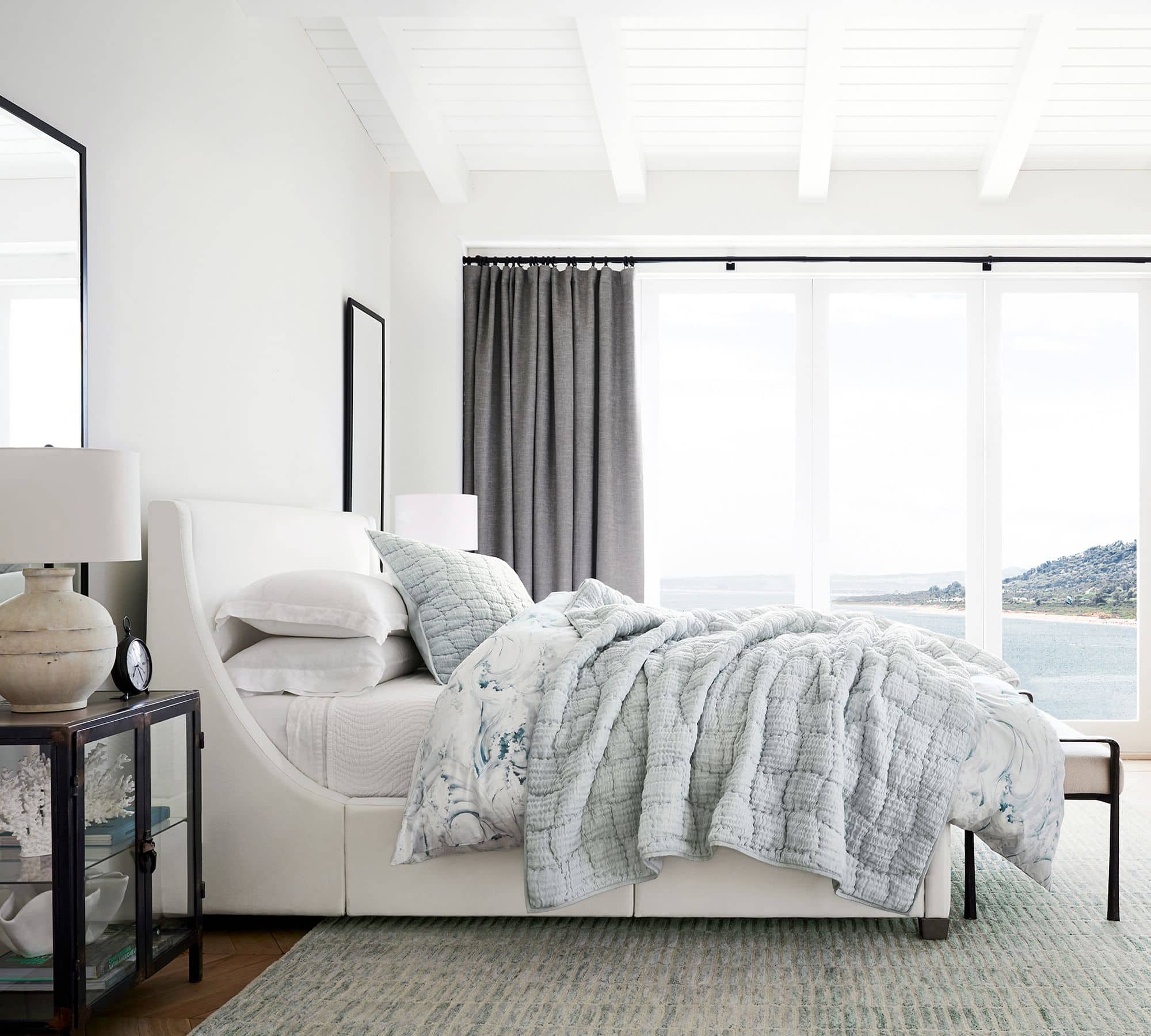 light blue quilt with all white bedding, white upholstered headboard