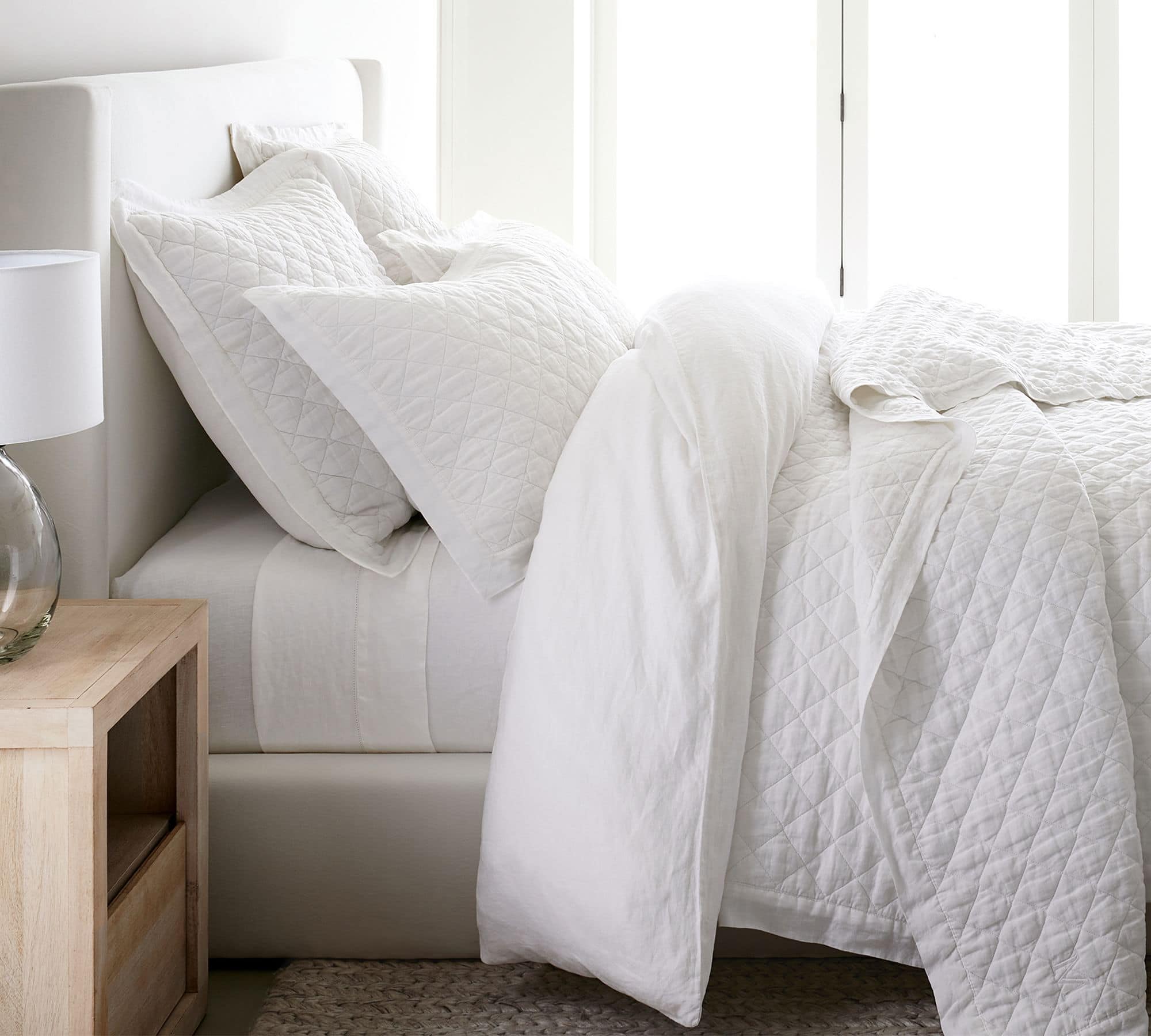 white quilt and matching euro shams on white upholstered bed.