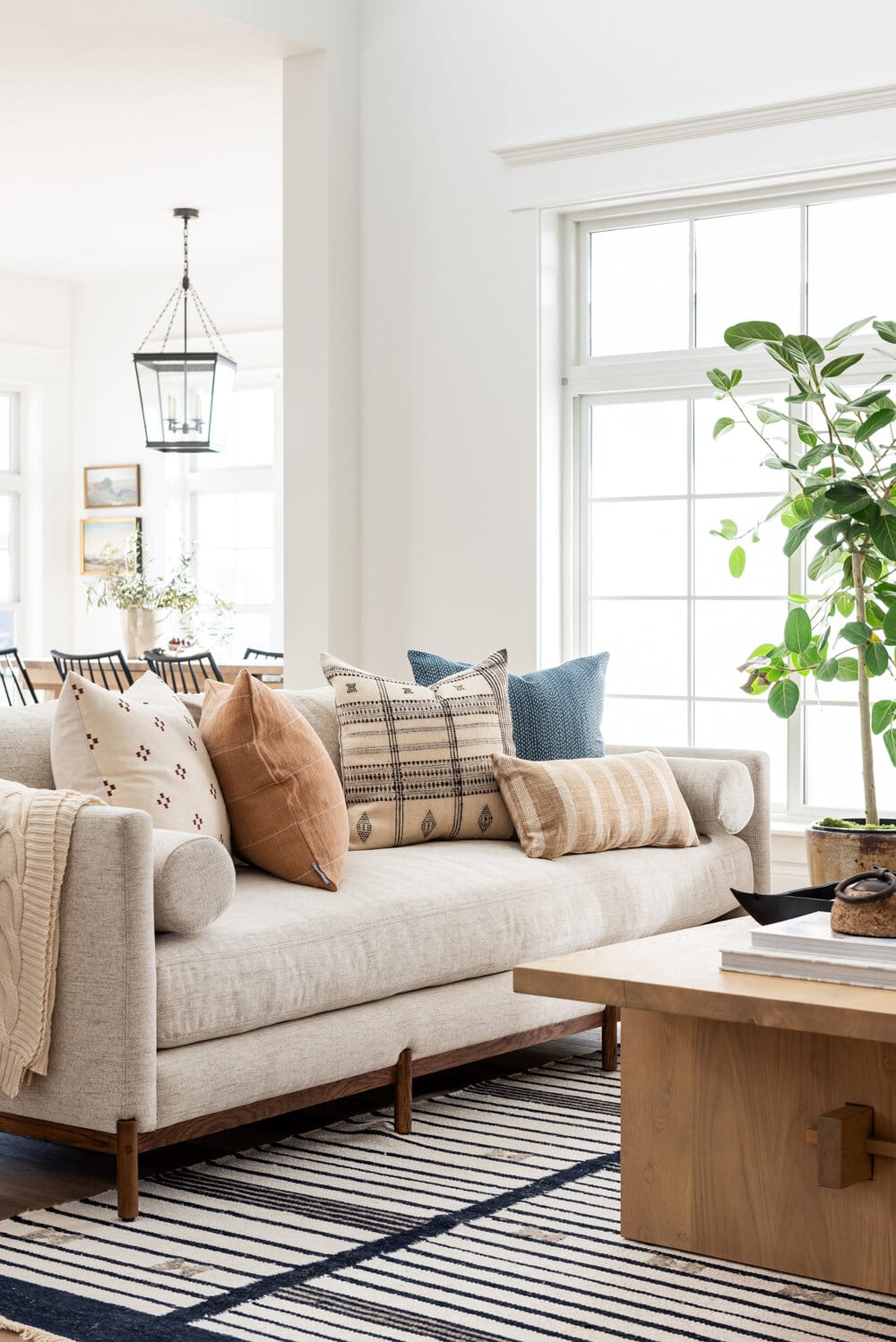 Soft cream paint color on walls with black hanging lantern, black spindle side chairs, tan colored sofa