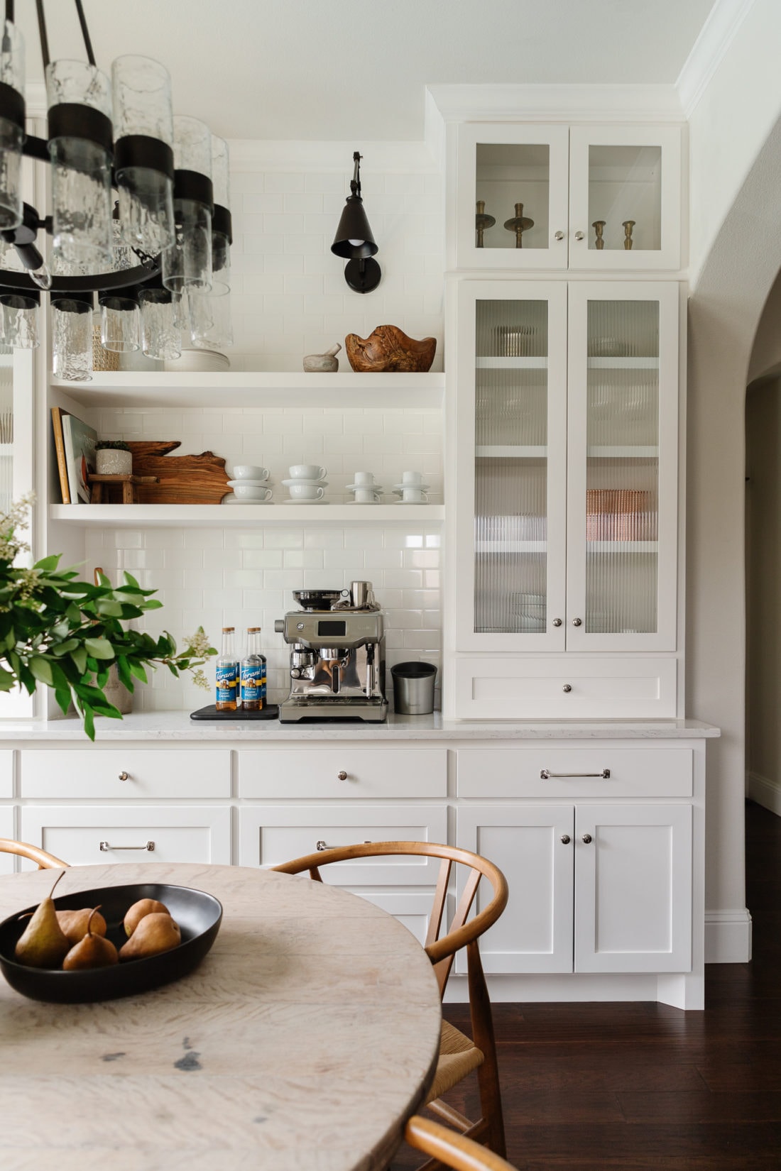 a side counter in a kitchen holds an espresso machine and coffee syrups on a tray