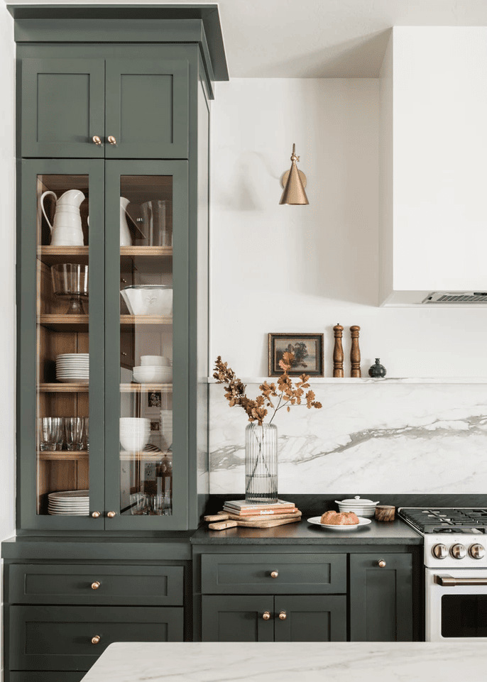 Dark forest green kitchen cabients with gold sconce lighting on either side of hood