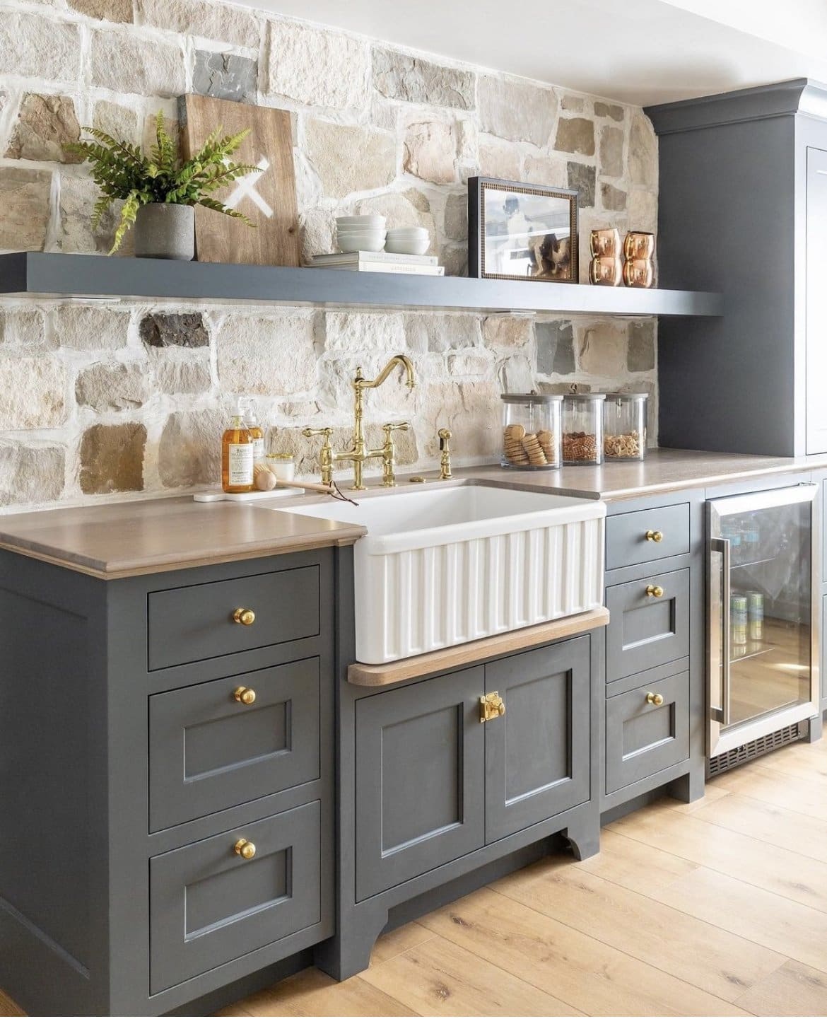 stone as the backsplash, dark grey cabinets, gold cabinet hardware, white farmhouse sink