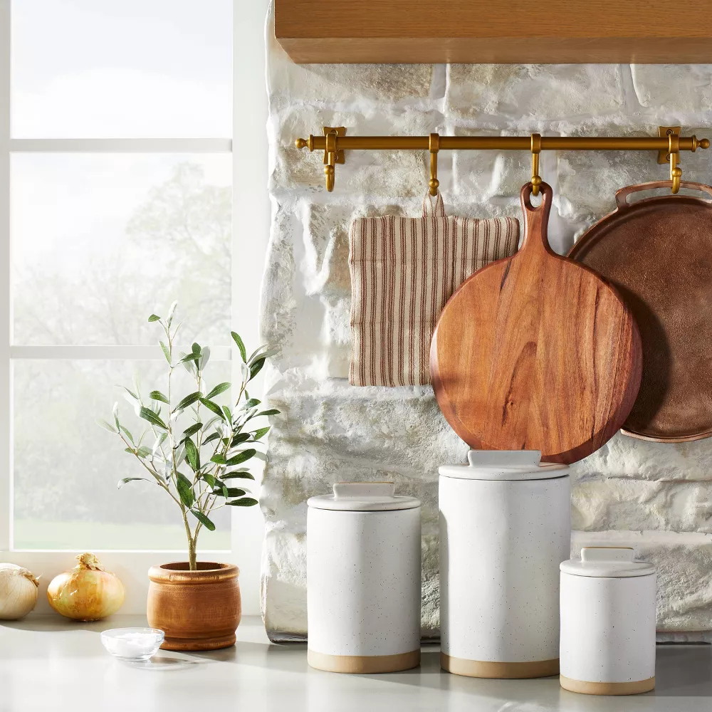 white canisters on a kitchen counter with a small olive tree in a pot.