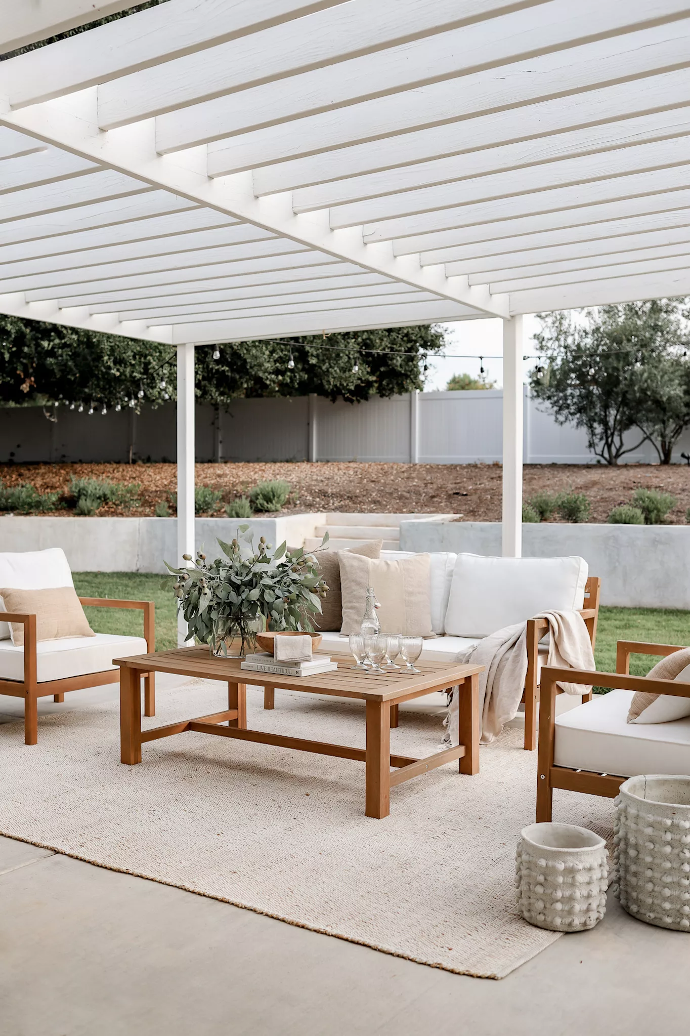 white pergola with teak outdoor patio sofa and chairs